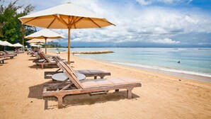 A beach with sun loungers and umbrellas, a clear sky, and a calm sea. - Hotel ZIA Bali - Kuta (Kuta)