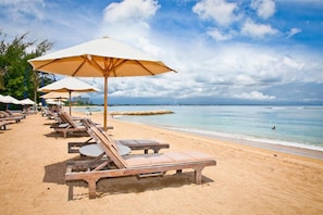 A beach with sun loungers and umbrellas, a clear sky, and a calm sea.