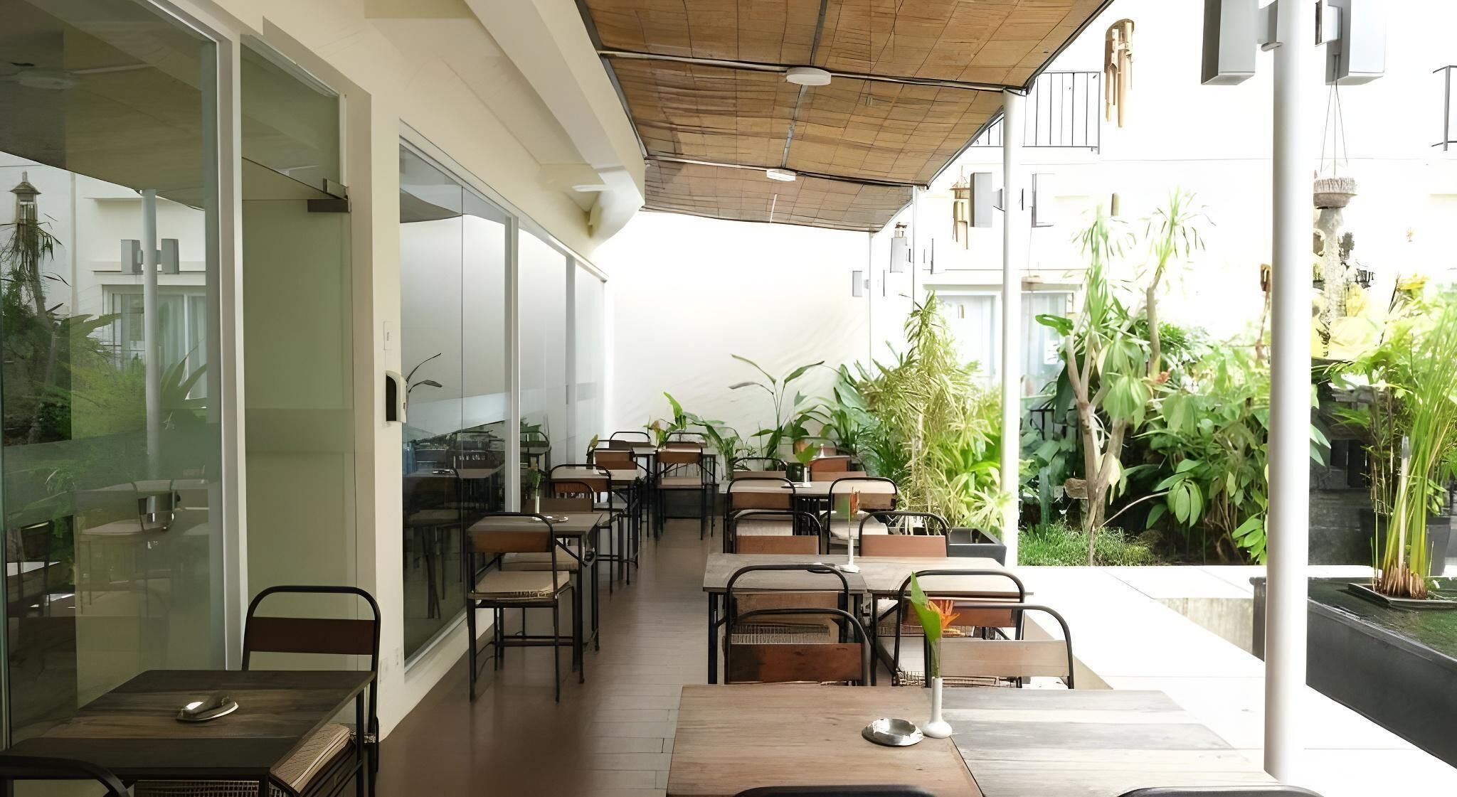 An outdoor dining area with tables and chairs, surrounded by glass walls and potted plants.