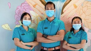Trois personnes vêtues d’uniformes turquoise se tiennent devant un mur orné d’un grand motif floral aux couleurs vives.