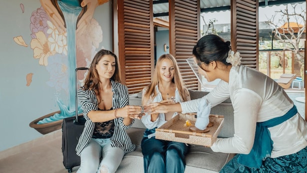 A group of people sitting on a couch, a tray with food and drinks, and a decorative wall with floral patterns. - Amolas Canggu Villa Balinese Muralism (Canggu)