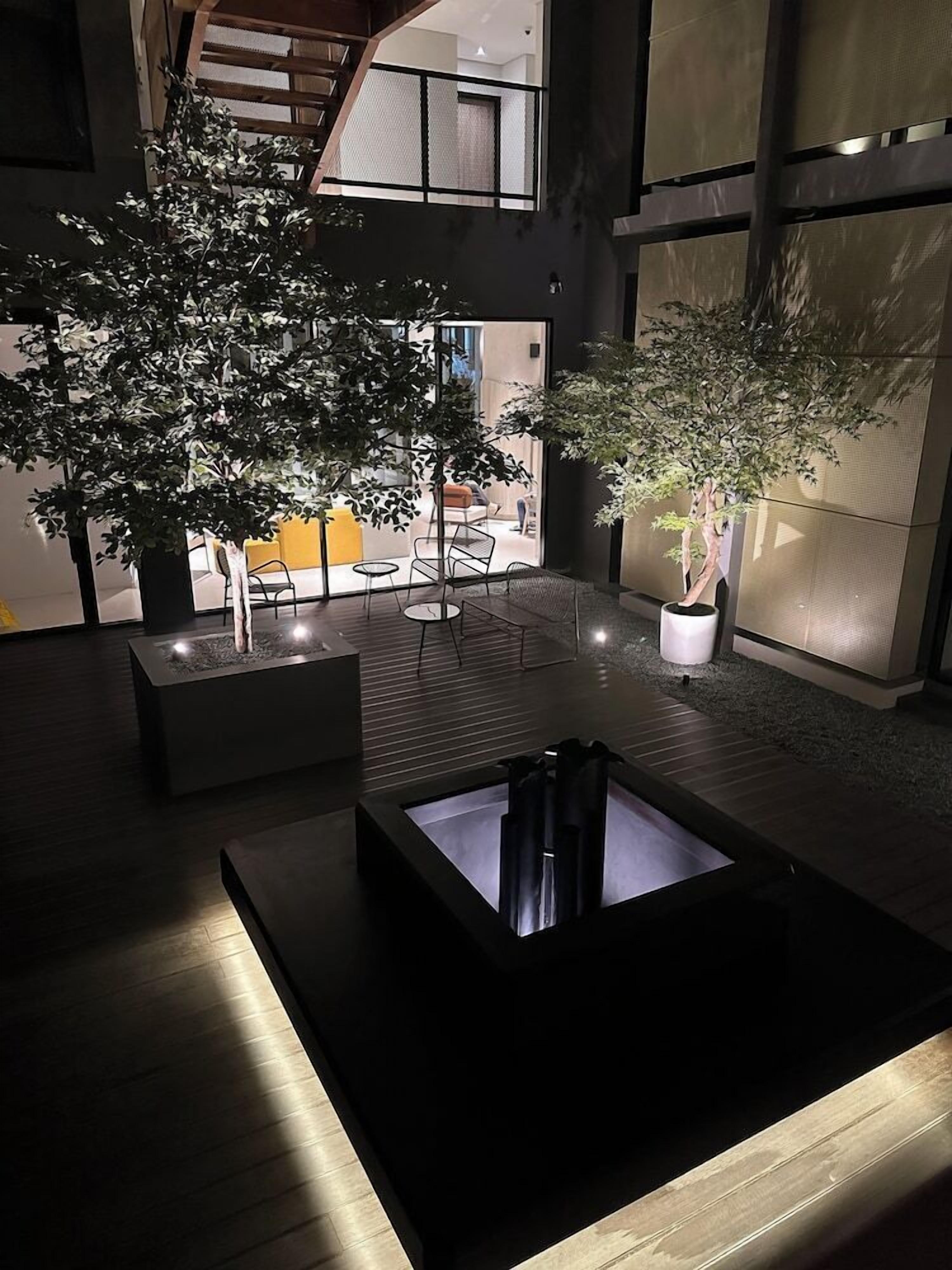 A modern indoor space with a central seating area, potted plants, and a view of the outside.
