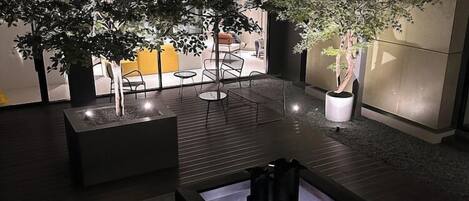 A modern indoor space with a central seating area, potted plants, and a view of the outside.