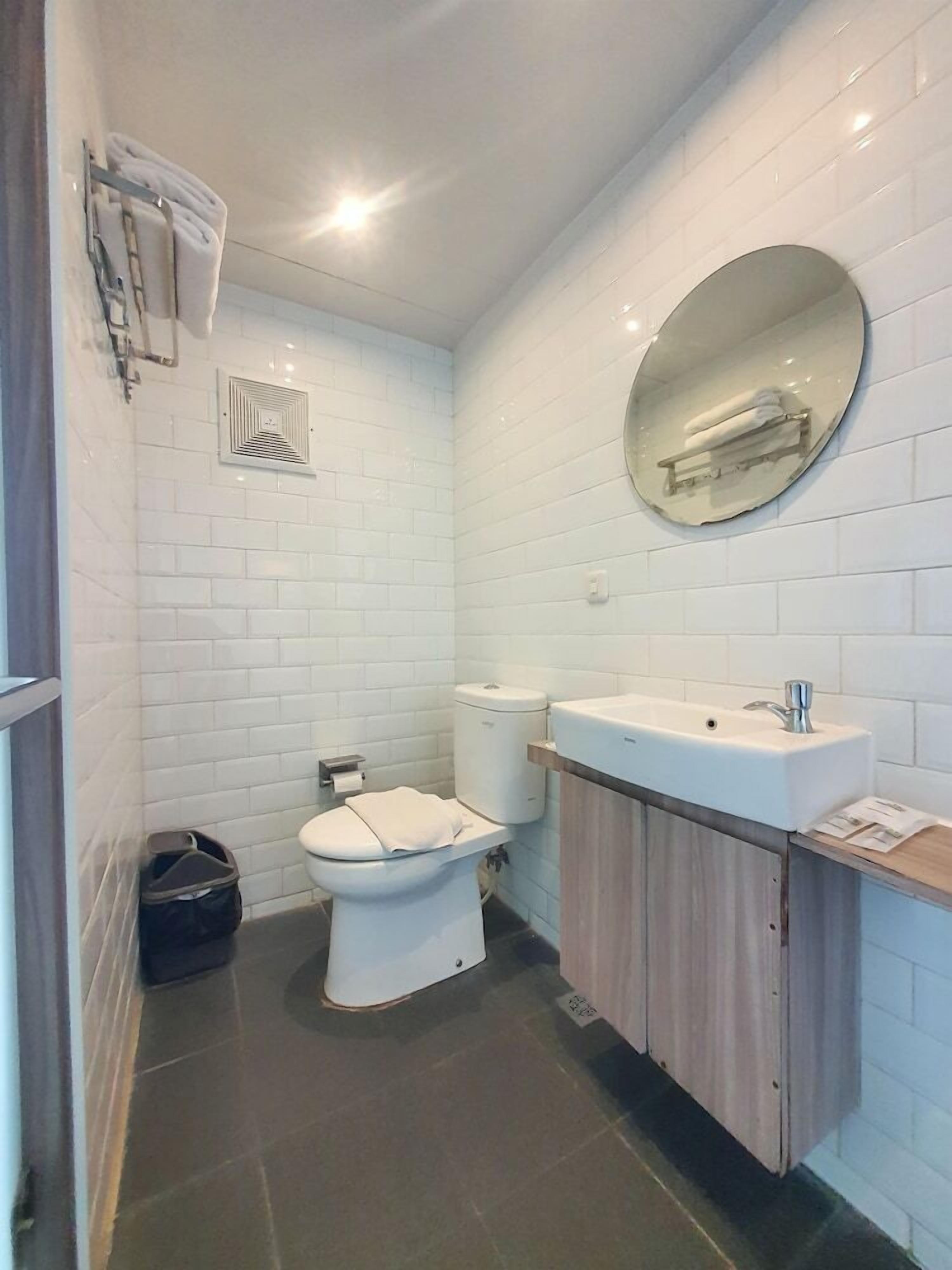 Un baño pequeño y moderno con azulejos blancos, inodoro, lavabo y espejo.