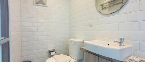 Un baño pequeño y moderno con azulejos blancos, inodoro, lavabo y espejo.