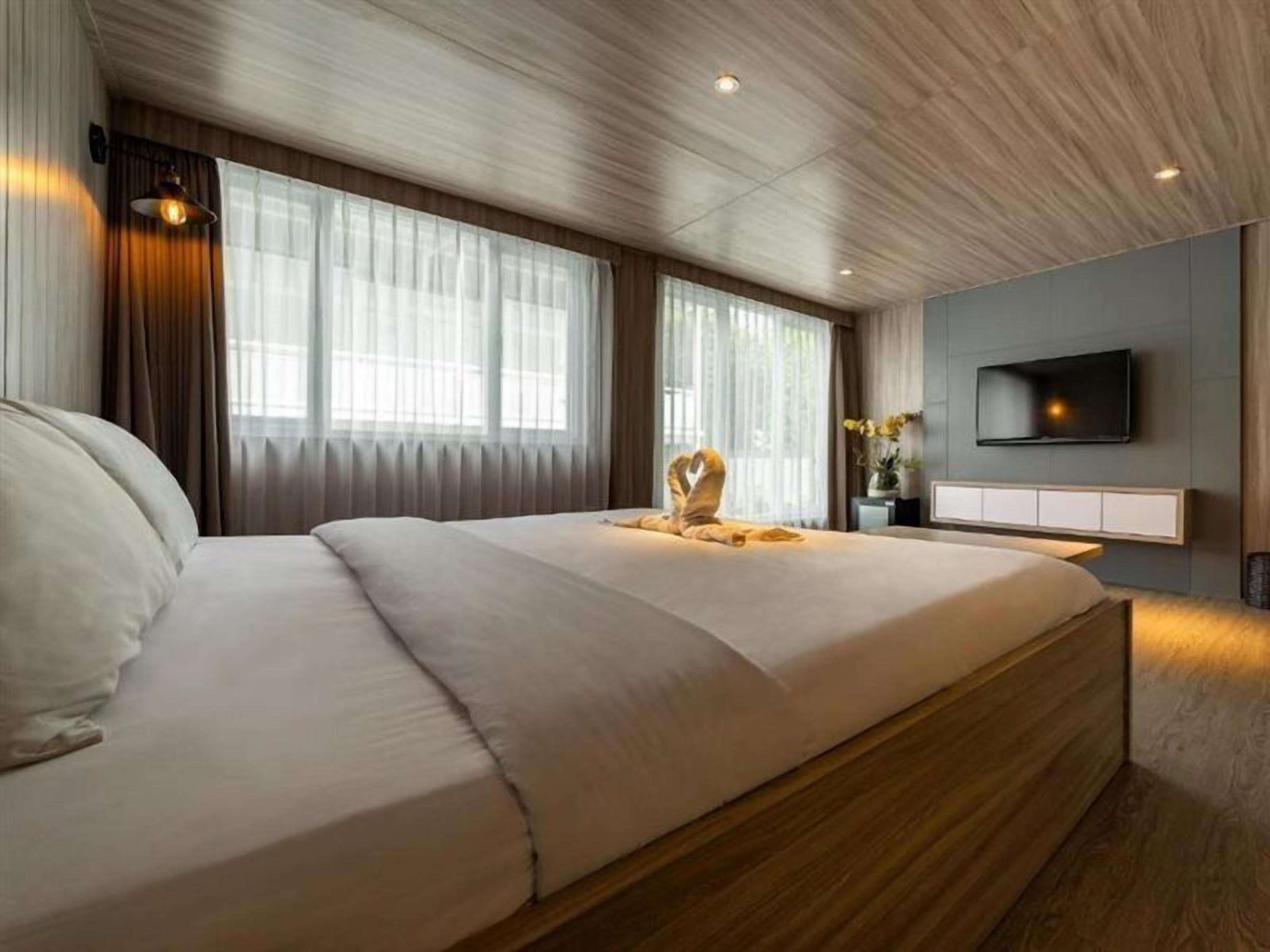Una camera d'albergo moderna con un letto grande, soffitto in legno e una TV a schermo piatto montata a parete.