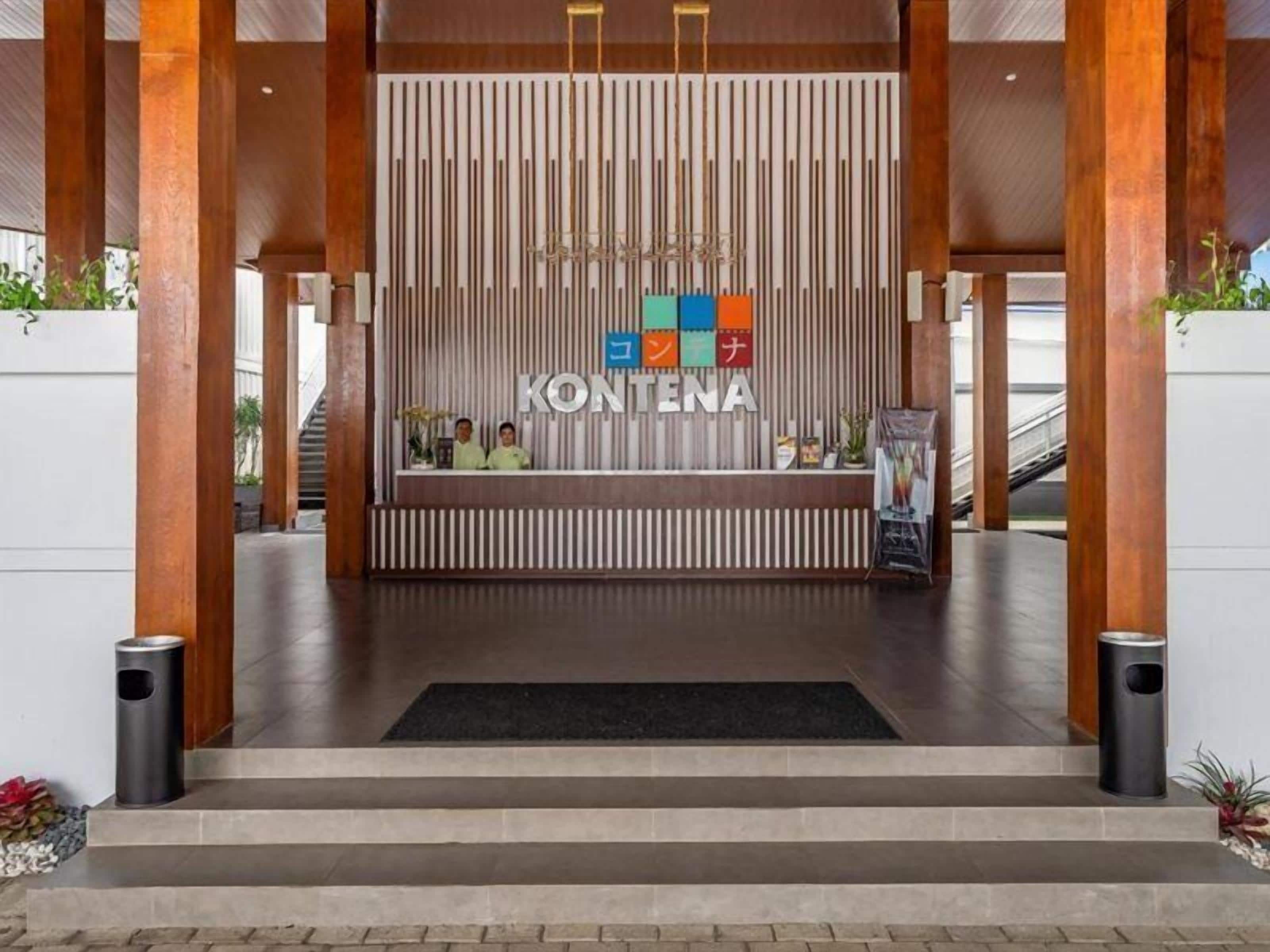 A reception area with a modern design, featuring a reception desk, a vertical wooden panel, and a chandelier.