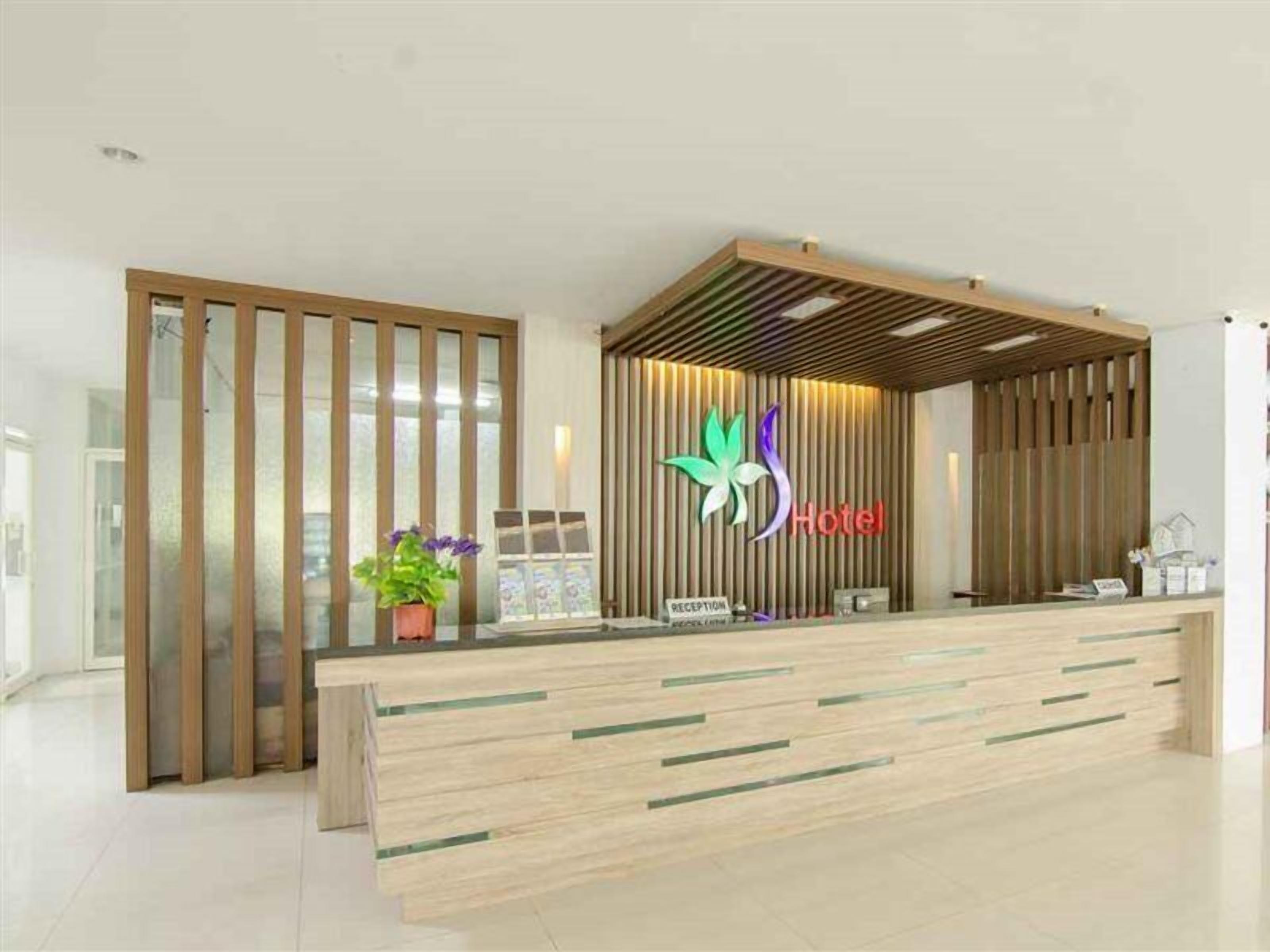 A hotel reception desk with a modern design, featuring a wooden reception area, a logo with a stylized flower, and a reception sign.