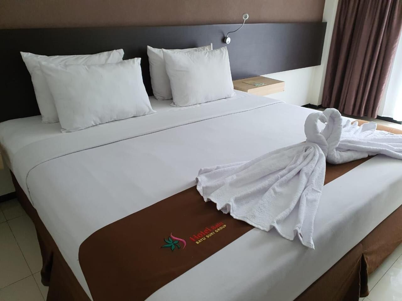 Una habitación de hotel con una cama bien hecha, cabecera marrón y un corredor de cama marrón con un logo.