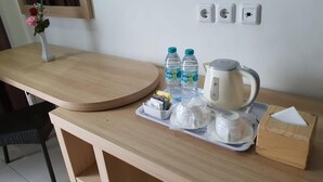 A hotel room with a wooden desk, a vase with flowers, two water bottles, a kettle, a tray with tissues, and a box of tissues. - Batu Suki Resort and Hotel (Batu)