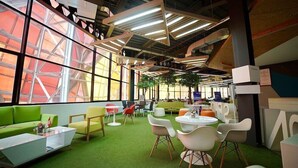 Un interior moderno con alfombra verde, muebles blancos y amarillos, y ventanas amplias.