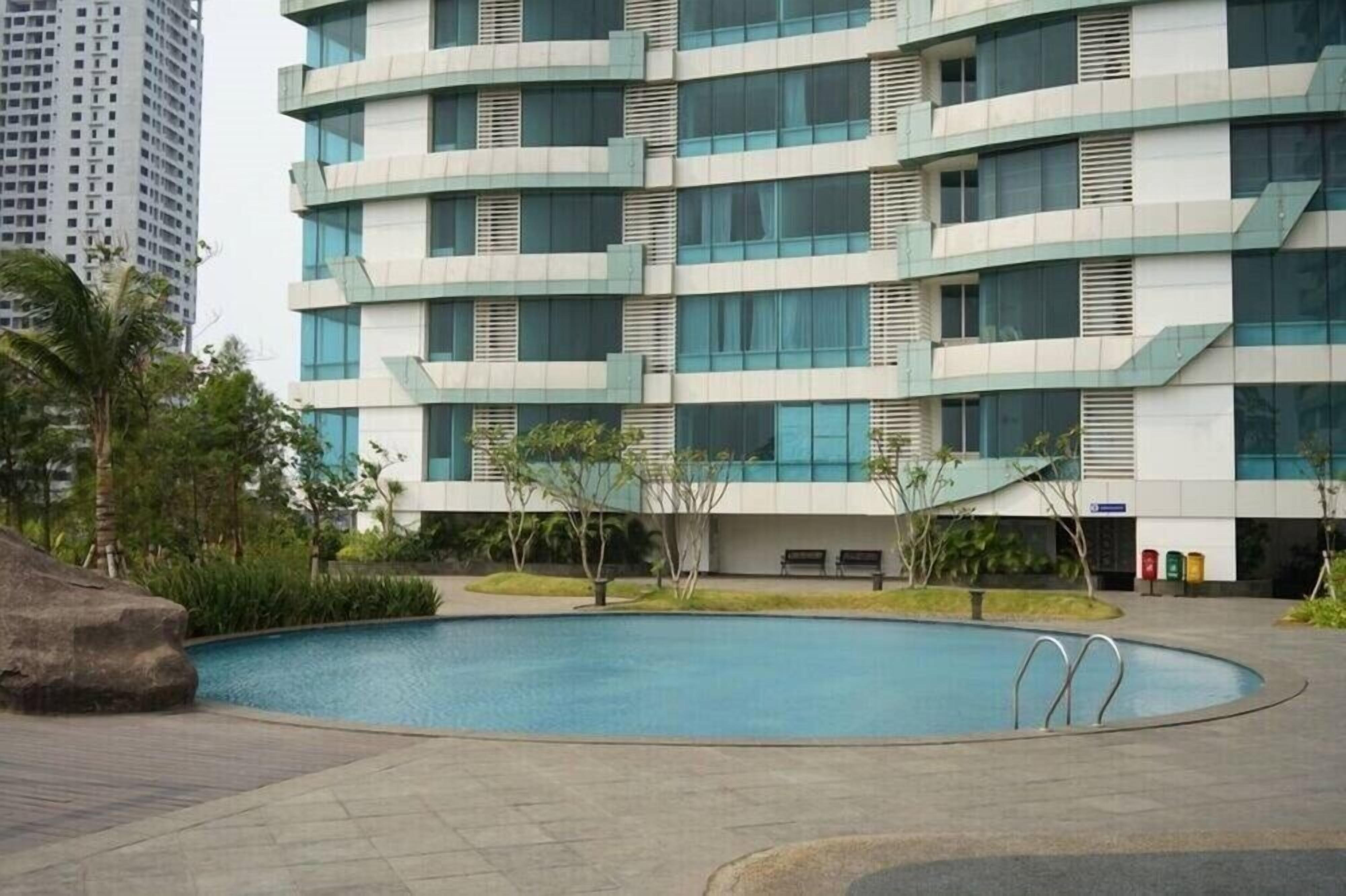 A modern building with a pool area, featuring a curved pool and a landscaped garden with small trees and shrubs.