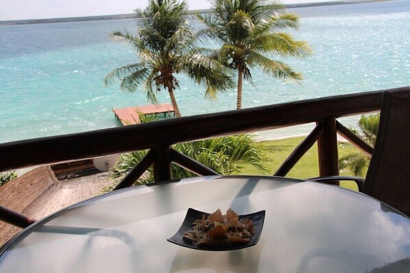 A table with a plate of food, overlooking a beach with palm trees and the ocean. - Zelune Luxury Lagoon Resort Bacalar Only Adults (Bacalar)