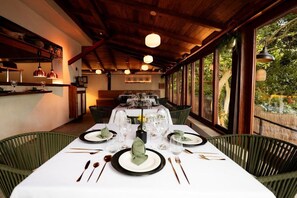 A dining area with a white table set for four, surrounded by green chairs, under wooden beams with hanging pendant lights. - Zelune Luxury Lagoon Resort Bacalar Only Adults (Bacalar)