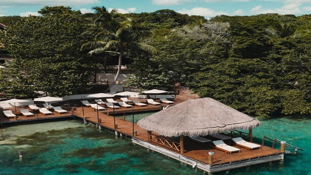 Wasserbungalows mit Strohdächern, Holzdecks und Liegestühlen.