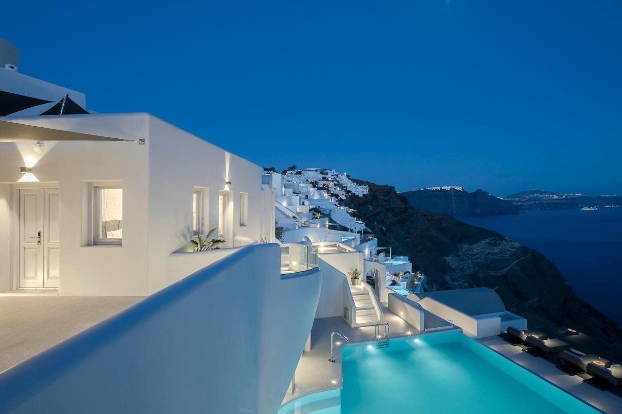 A modern white building with a pool and a view of a coastal cliff.