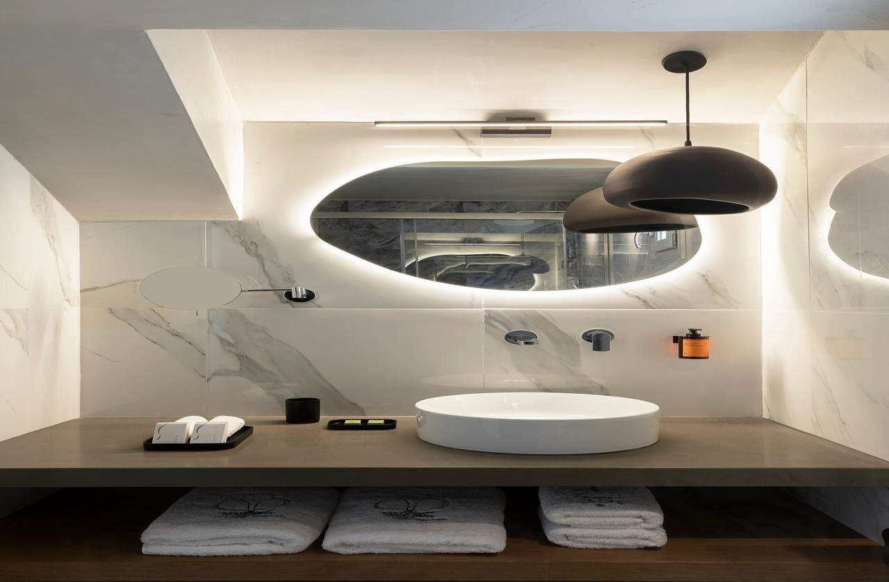 Un bagno moderno con un lavandino rotondo, uno specchio e una lampada a sospensione.