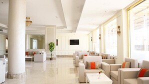 Een ruime hotellobby met een modern design, voorzien van een groot zitgedeelte met banken en fauteuils, een flatscreen televisie aan de muur en grote ramen voor natuurlijk licht.