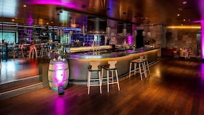 Un espace bar moderne comprenant un comptoir, des tabourets et un grand tonneau illuminé.