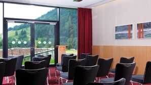 Une salle de conférence avec des chaises noires, un pupitre et une grande fenêtre donnant sur des collines verdoyantes.