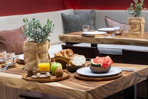 A breakfast setting with a wooden table, a bowl of fruit, a glass of orange juice, and a plant in a burlap sack. - Yelo Hotel (Nice)