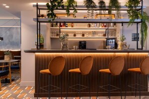 A bar area with a counter, bar stools, shelves with bottles, and hanging plants. - Ikonik Jean Medecin (Nice)