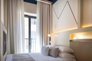 Una habitación de hotel moderna con una cama grande, cortinas, una lámpara de pared y vistas al exterior.