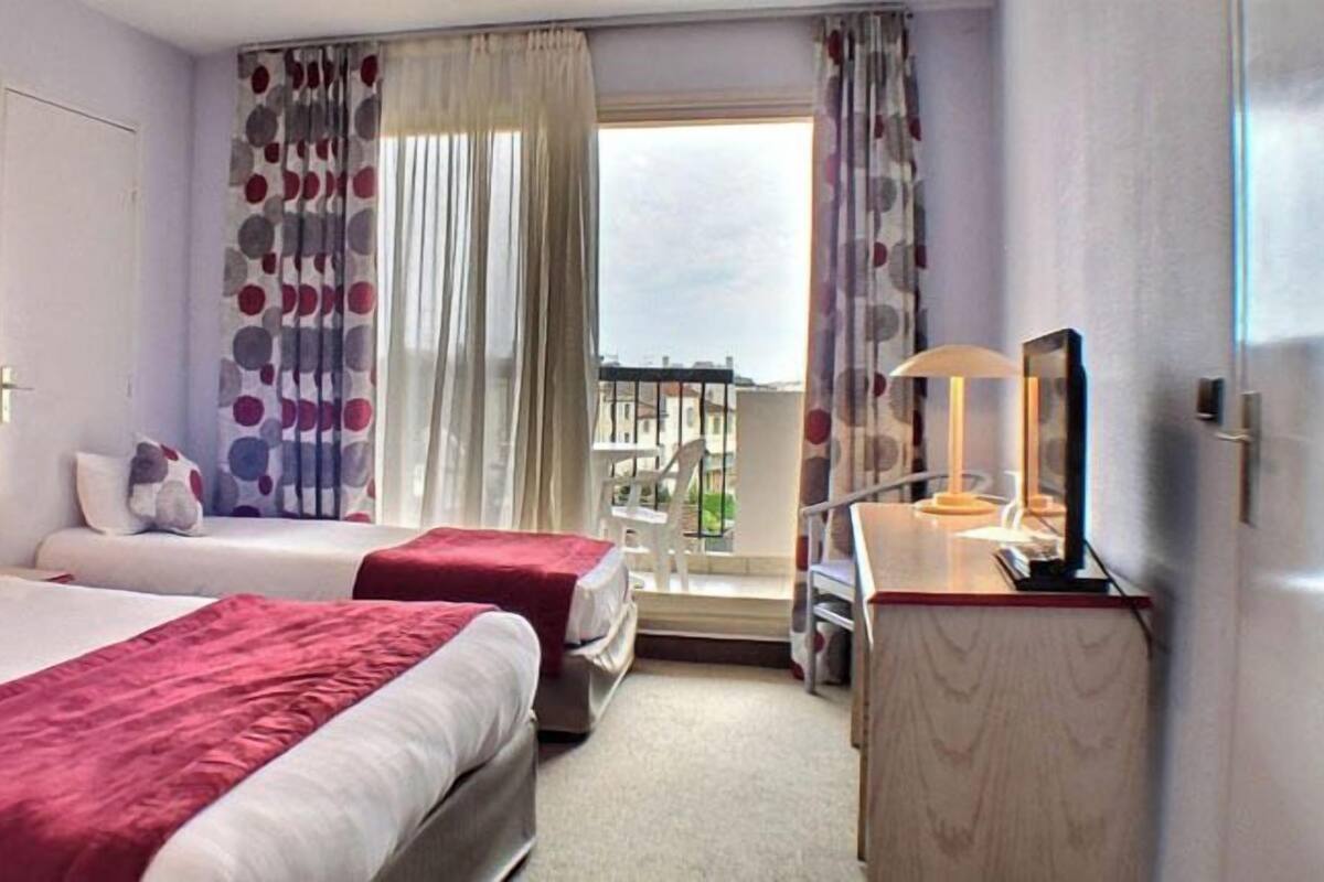 Une chambre d’hôtel avec deux lits, un bureau, une chaise, une télévision et un balcon avec vue.