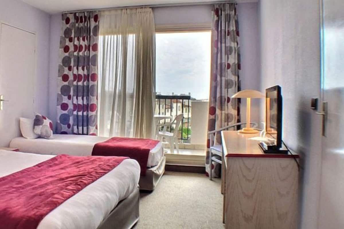 Habitación de hotel con dos camas, un escritorio, una silla, un televisor y un balcón con vistas.