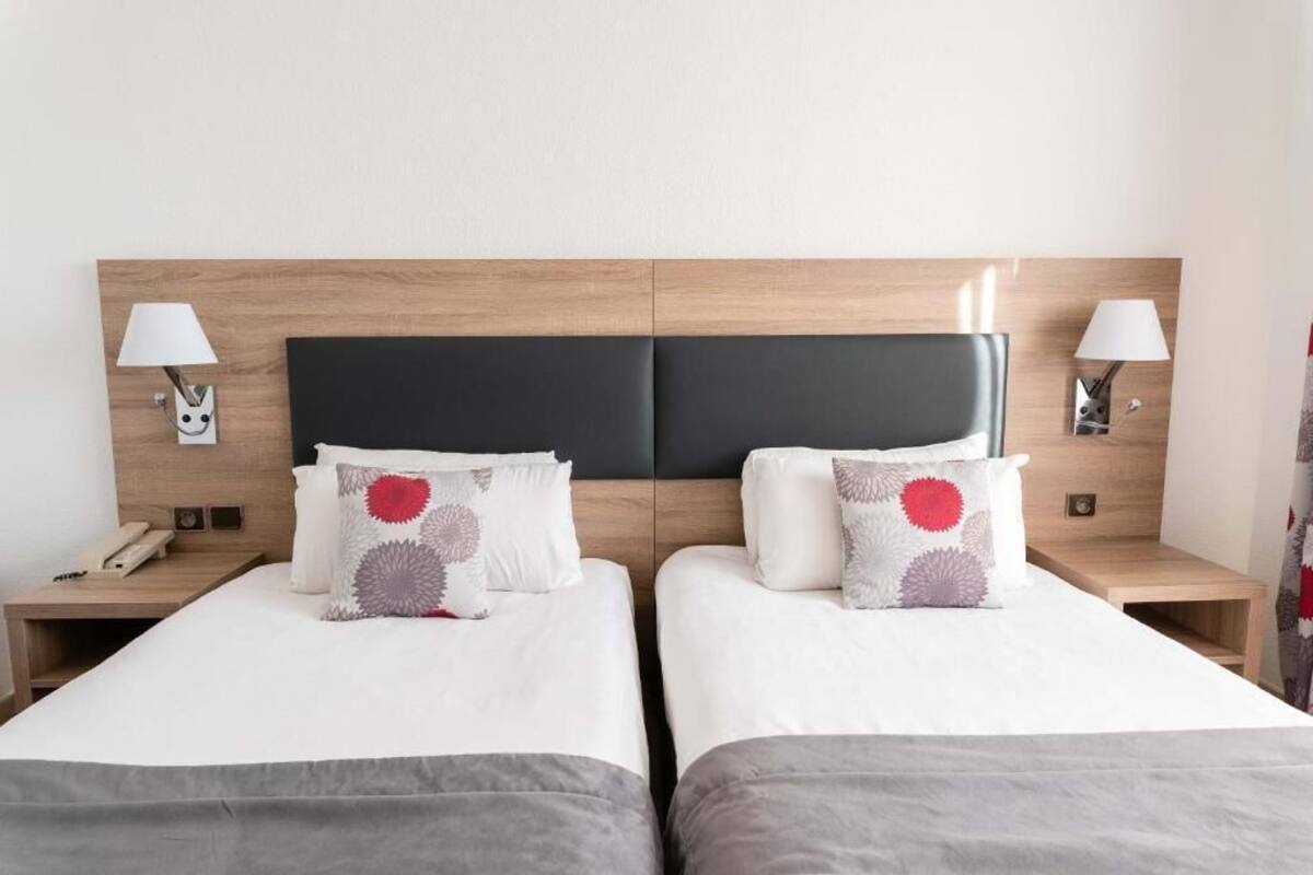 Une chambre d’hôtel avec deux lits, une tête de lit en bois, des lampes de chevet et un téléphone sur la table de chevet.