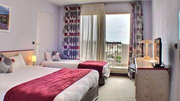 A hotel room with two beds, a desk, a chair, a TV, and a balcony with a view.