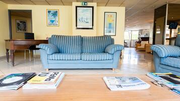 A lobby with a blue sofa, a wooden coffee table with magazines, a piano, and framed pictures on the wall.