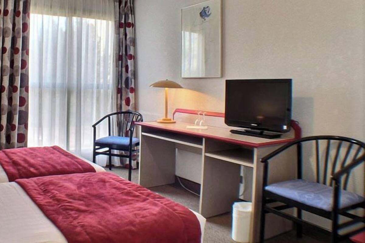 Une chambre d’hôtel avec deux lits, un bureau avec un ordinateur, une chaise et un téléviseur.