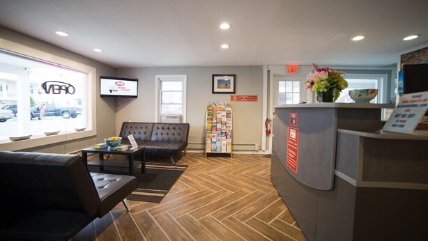A reception area with a sofa, a coffee table, a TV, a bulletin board, and a reception desk. - Wildwood Inn, a Travelodge by Wyndham (Wildwood)