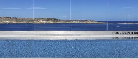 A swimming pool with a clear view of the sea and rocky coastline in the background.