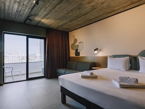 Een hotelkamer met een groot bed, een bank, een klein tafeltje en uitzicht op de stad door een schuifdeur.