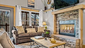 Un salon chaleureux avec une cheminée en pierre, un canapé en cuir et une grande fenêtre donnant sur une forêt.