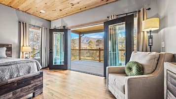 Un dormitorio con techo de madera, una cama, un sofá y un balcón con vistas a la montaña.