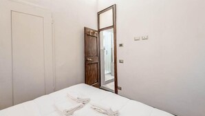 A bedroom with a bed, two towels, a wooden door, and a mirror.