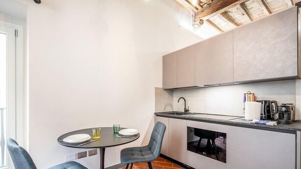 A compact kitchen with a dining table and chairs, a built-in oven, and a coffee machine.