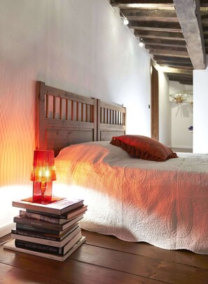 A bedroom with a wooden headboard, a stack of books, a red lamp, and a white textured bedspread. - A Few Steps to The Duomo Amazing 4BD Apt (Florence)