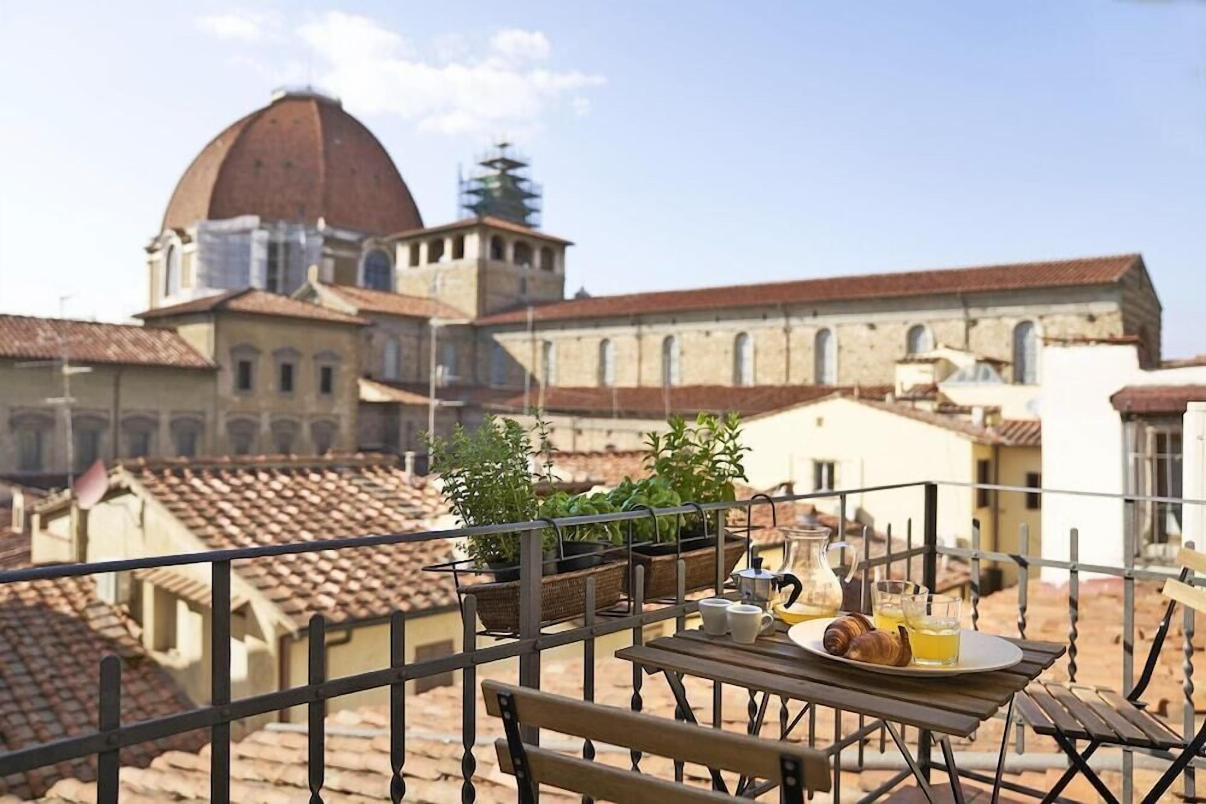 A balcony with a table set for breakfast, overlooking a historic building with a dome and arches.