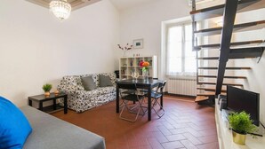 A living room with a sofa, a dining table with chairs, a chandelier, a bookshelf, and a staircase. - Della Scala Modern Apartment (Florence)