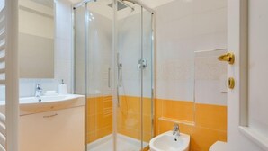 A bathroom with a glass-enclosed shower, a sink, and a bidet.