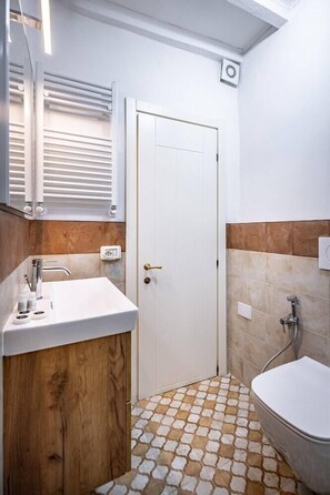 A bathroom with a white sink, wooden vanity, a white door, and a patterned floor. - Flospirit - Viola (Florence)