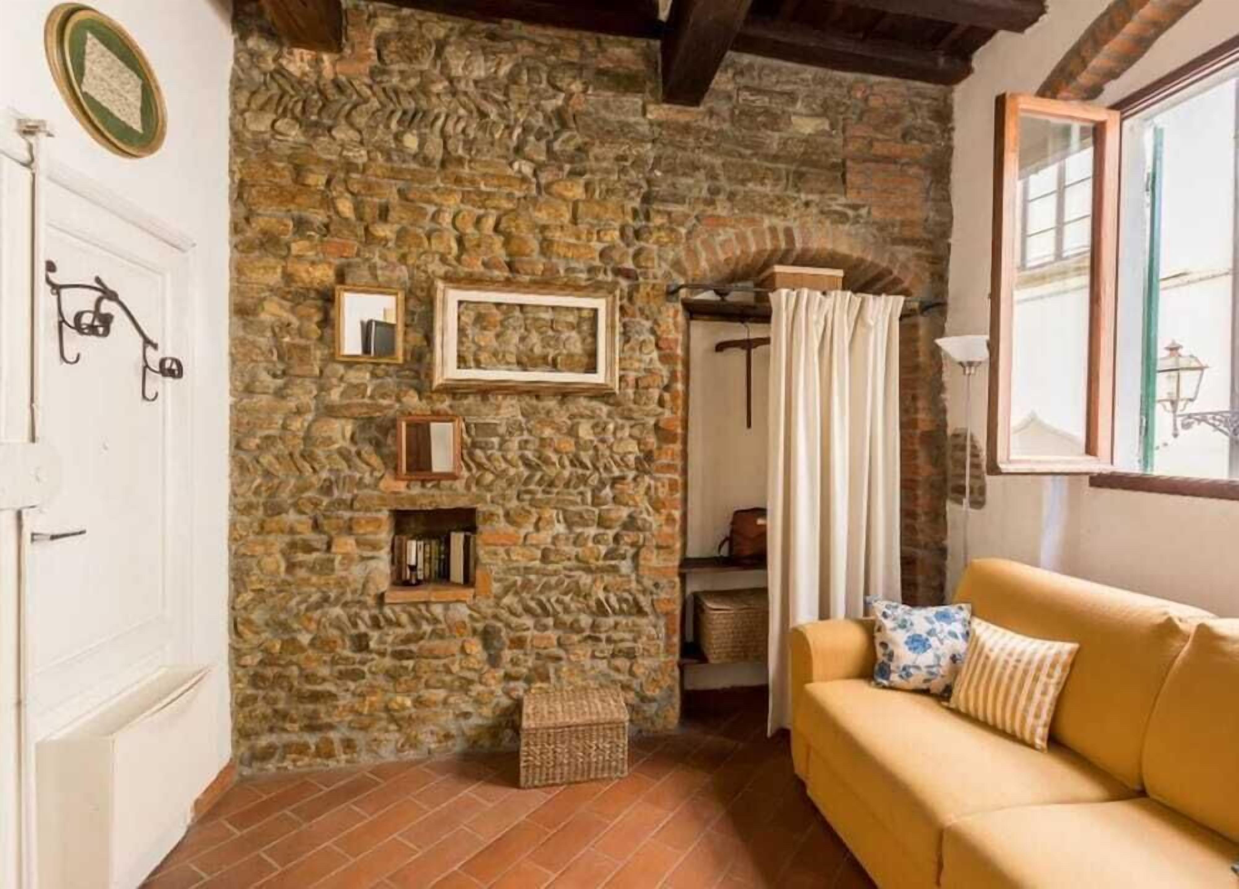 A cozy room with a stone wall, a white door, a yellow sofa, and a window with a view.
