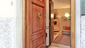 A wooden door with a metal ring handle, leading into a room with a patterned rug, a sofa, and framed pictures on the wall. - Ghibellina Apartment (Florence)