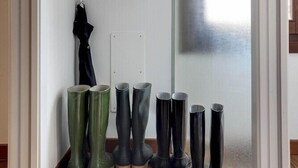 A room with a wooden floor, a white cabinet with two doors, and several pairs of boots and vases arranged against the wall. - Residenza Valier (Venice)