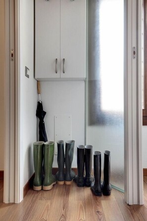A room with a wooden floor, a white cabinet with two doors, and several pairs of boots and vases arranged against the wall. - Residenza Valier (Venice)