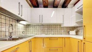 A kitchen with white upper cabinets, yellow lower cabinets, a stainless steel sink, and a tiled backsplash. - Residenza Valier (Venice)